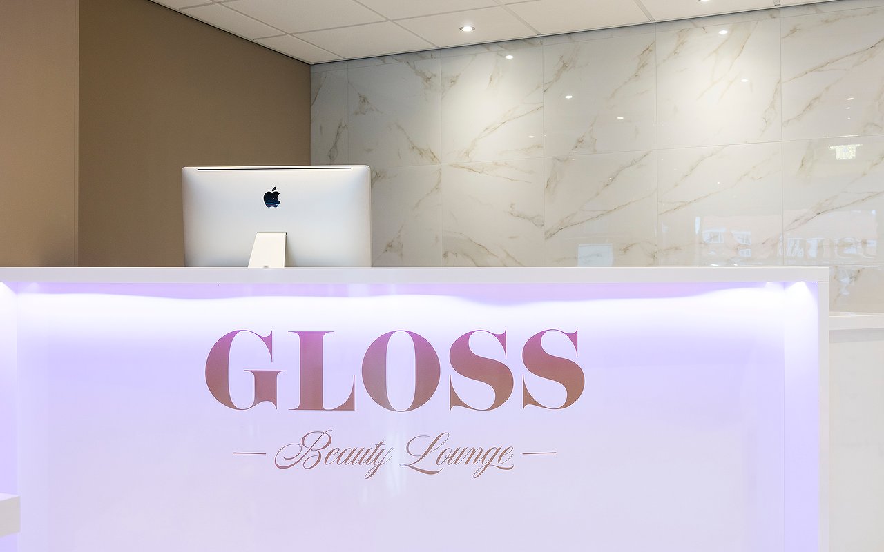 De verlichte balie met het GLOSS Beauty Lounge-logo en de marmeren wand